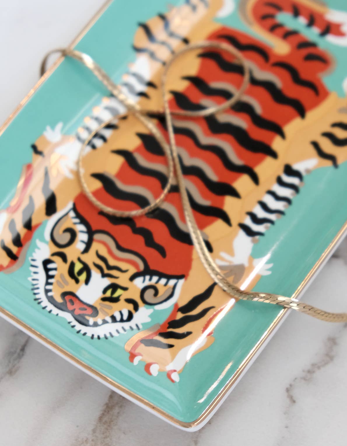 Teal decorative tray with a tiger design and gold accents on a marble surface