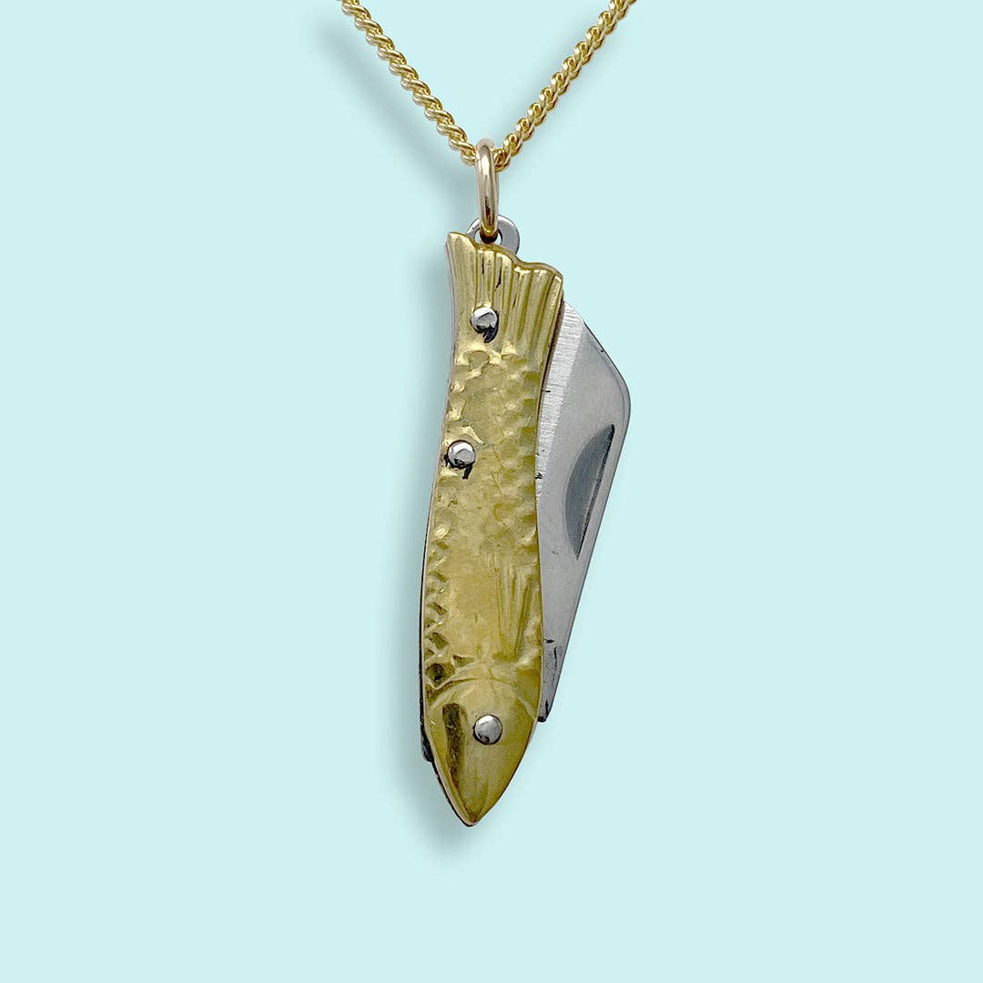 Gold and silver fish-shaped pendant on a gold chain against a light blue background
