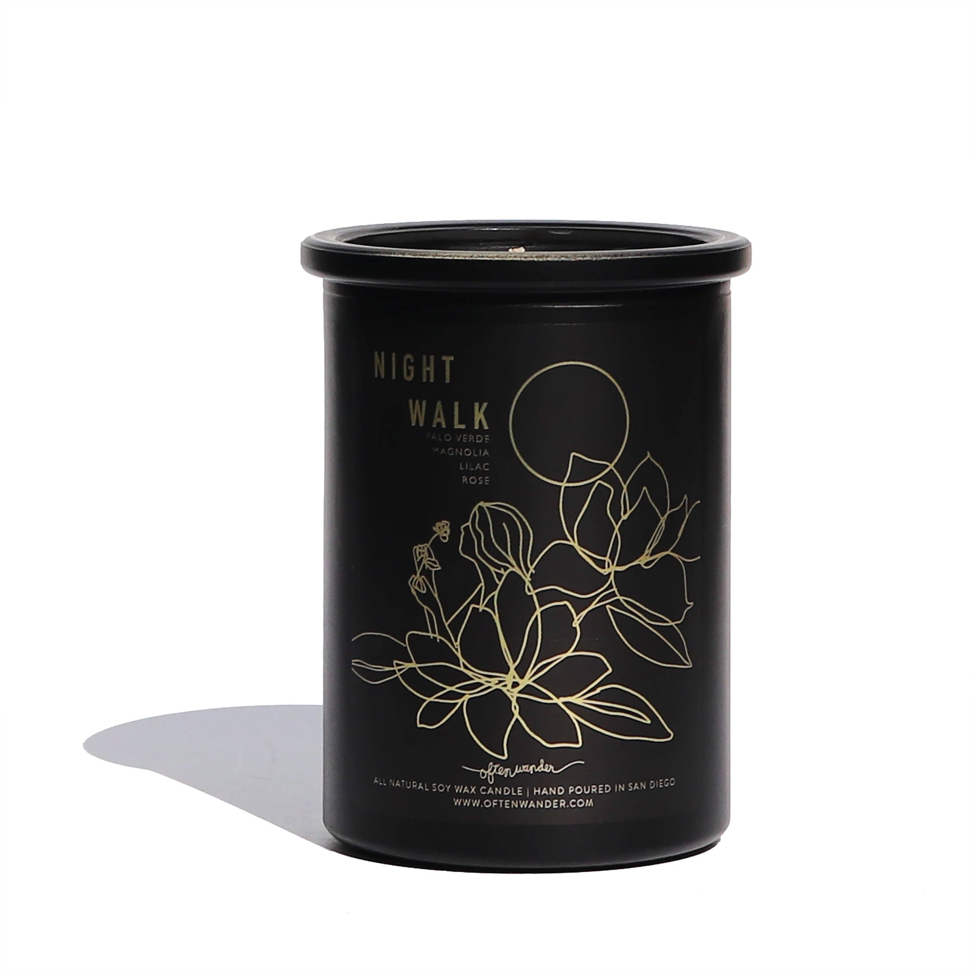 A black cylindrical soy wax candle jar with gold foil text reading 'NIGHT WALK' and a gold line drawing of flowers and a moon, photographed on a white background with a soft shadow.