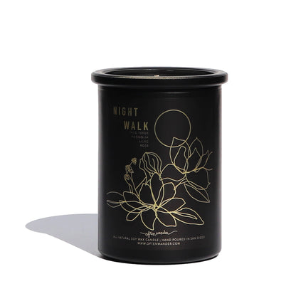 A black cylindrical soy wax candle jar with gold foil text reading 'NIGHT WALK' and a gold line drawing of flowers and a moon, photographed on a white background with a soft shadow.