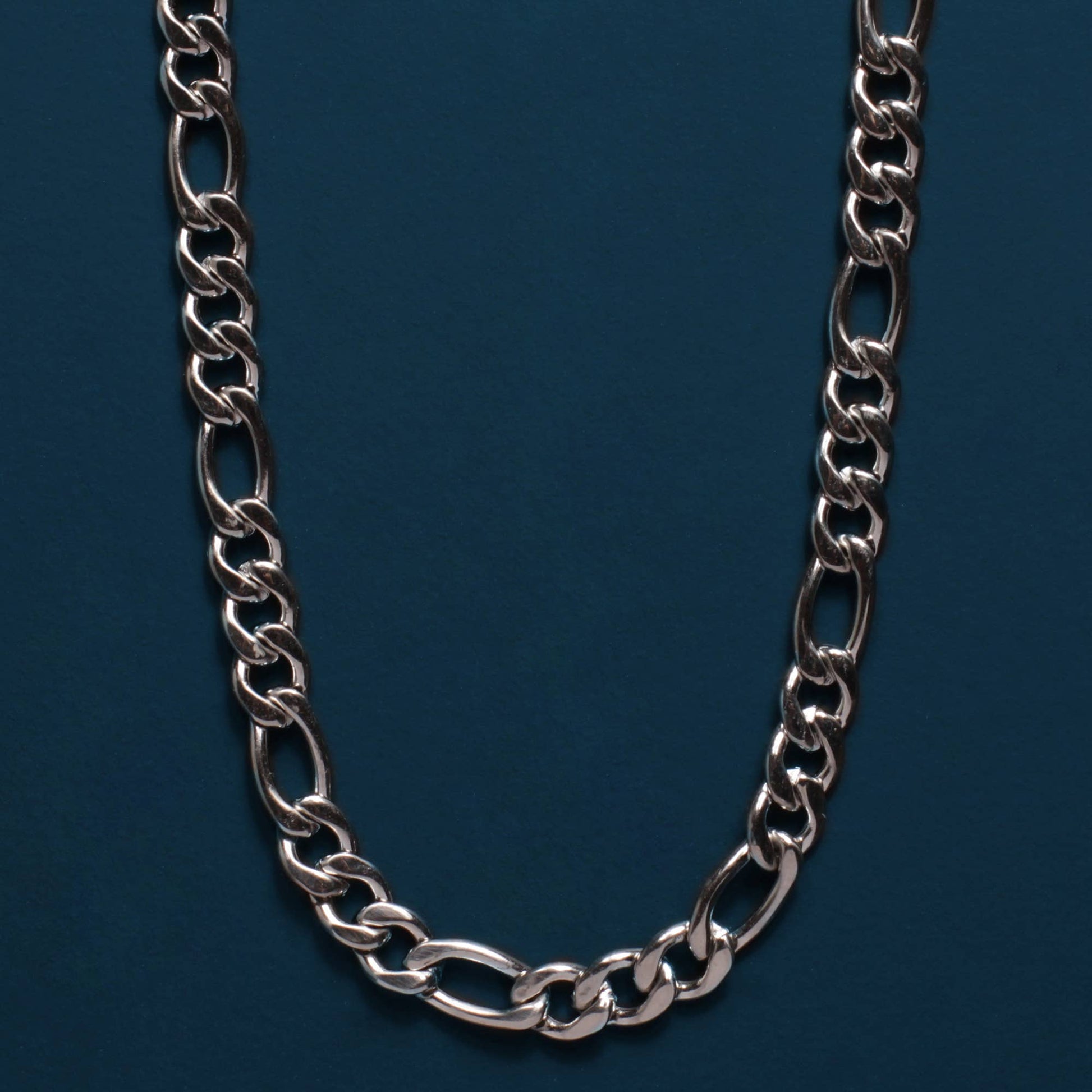 A silver-toned metal chain necklace with elongated oval links, arranged in a U-shape against a dark teal-blue background.