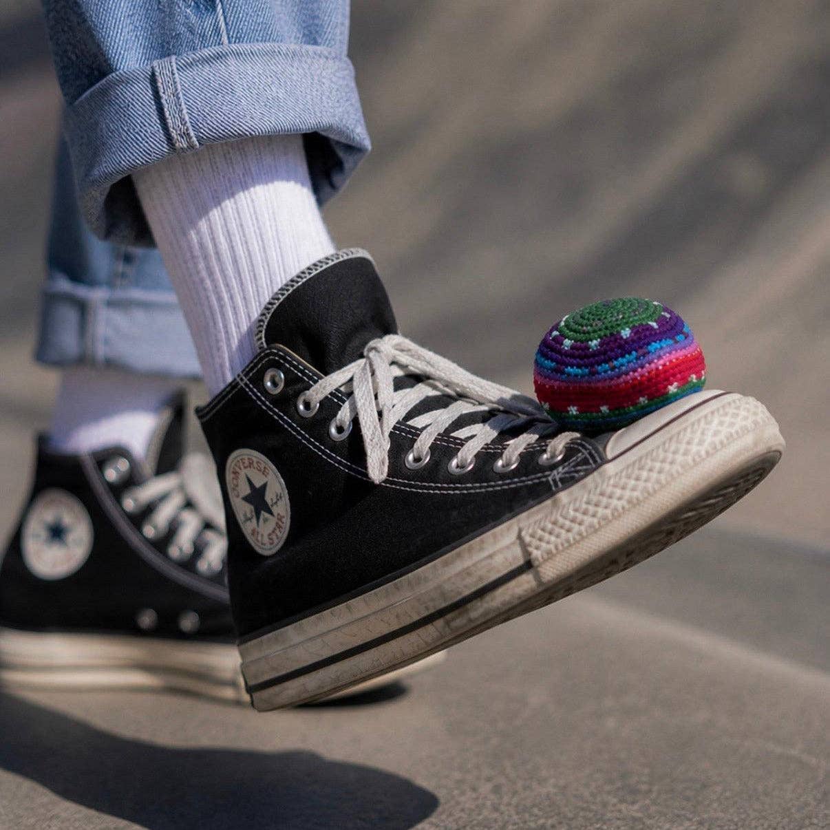 Person wearing black Converse sneakers with a colorful ball on a blurred background
