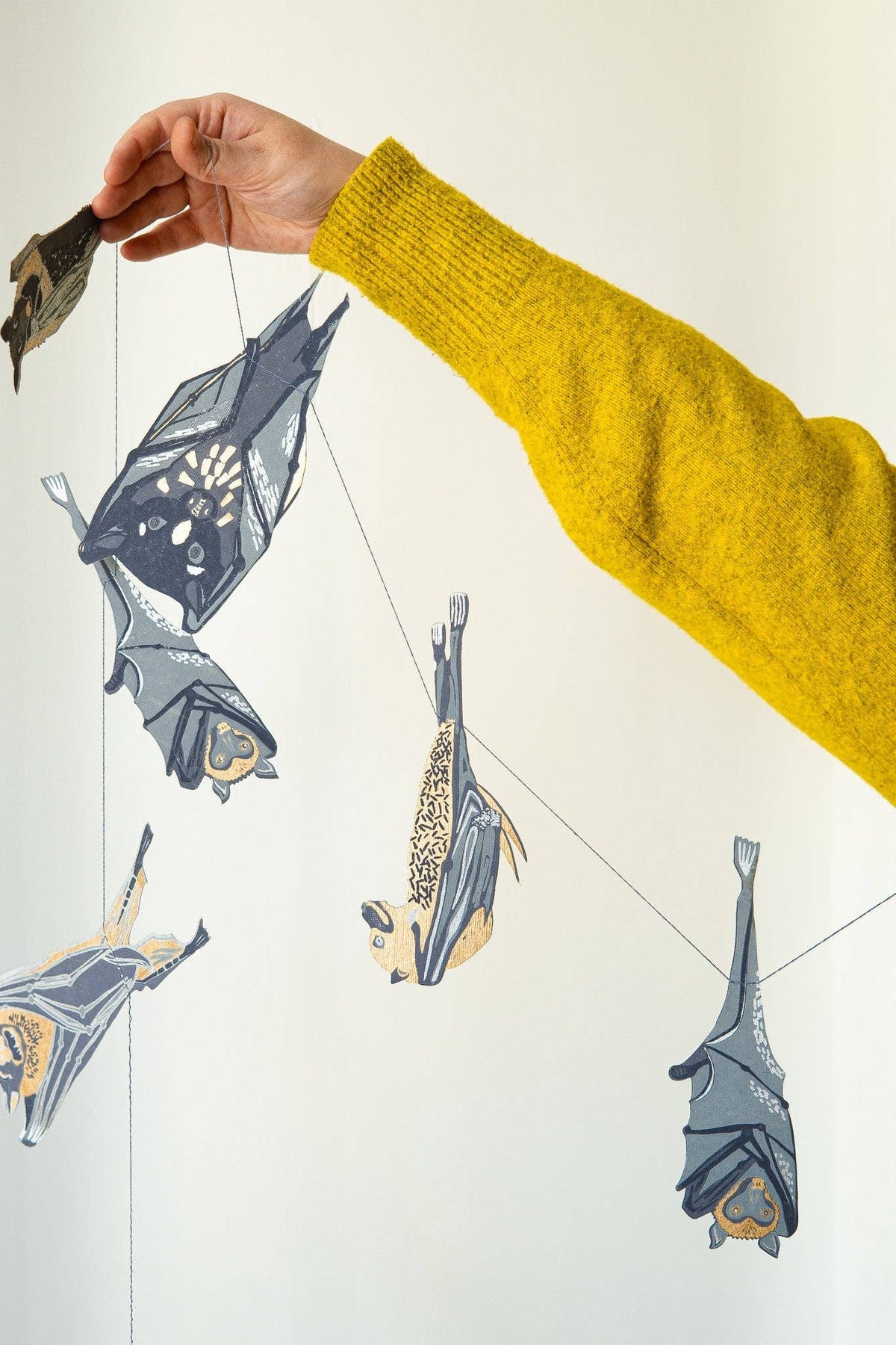 Hand holding a string with bat-shaped paper decorations against a white background