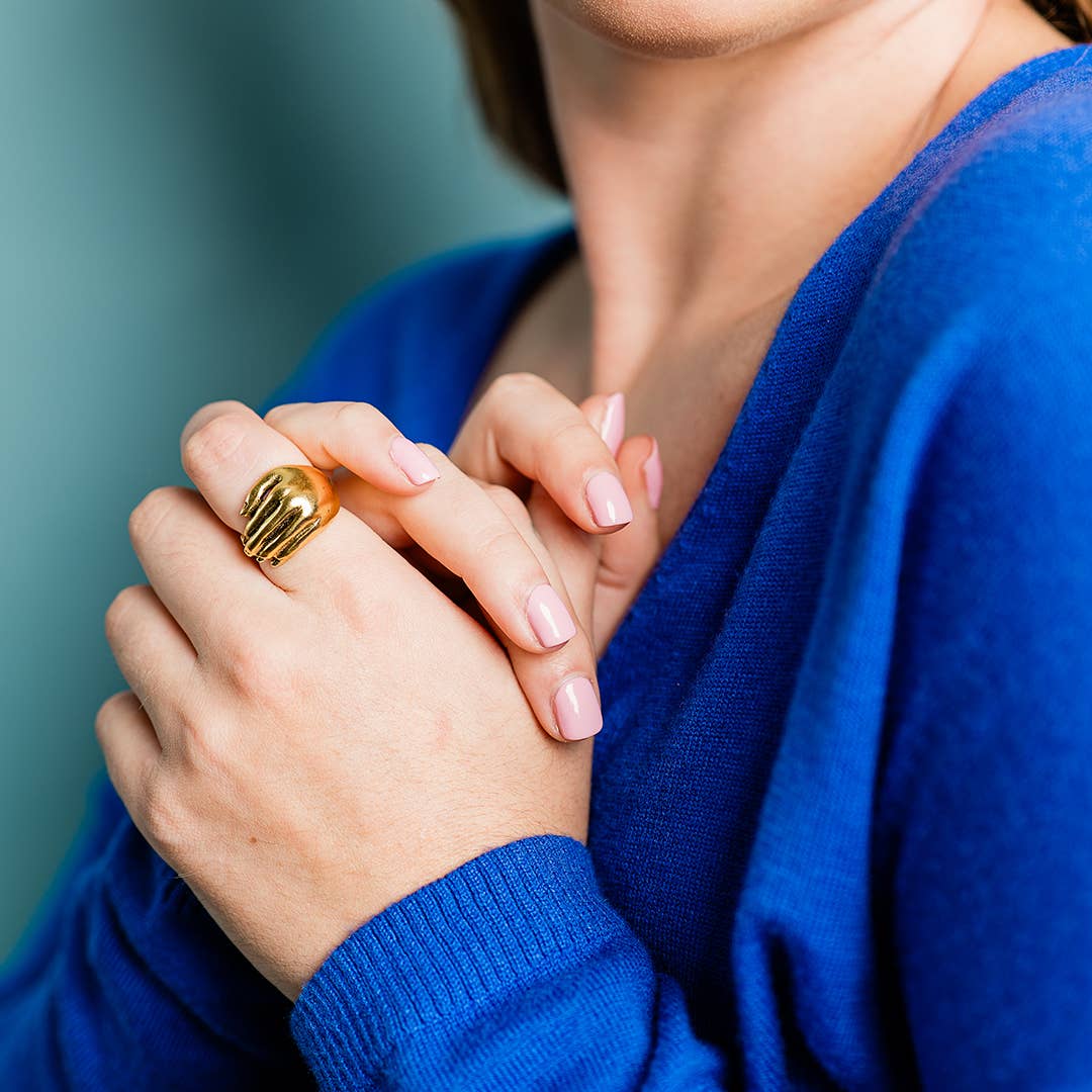 Person wearing a gold ring with a blue sweater against a teal background