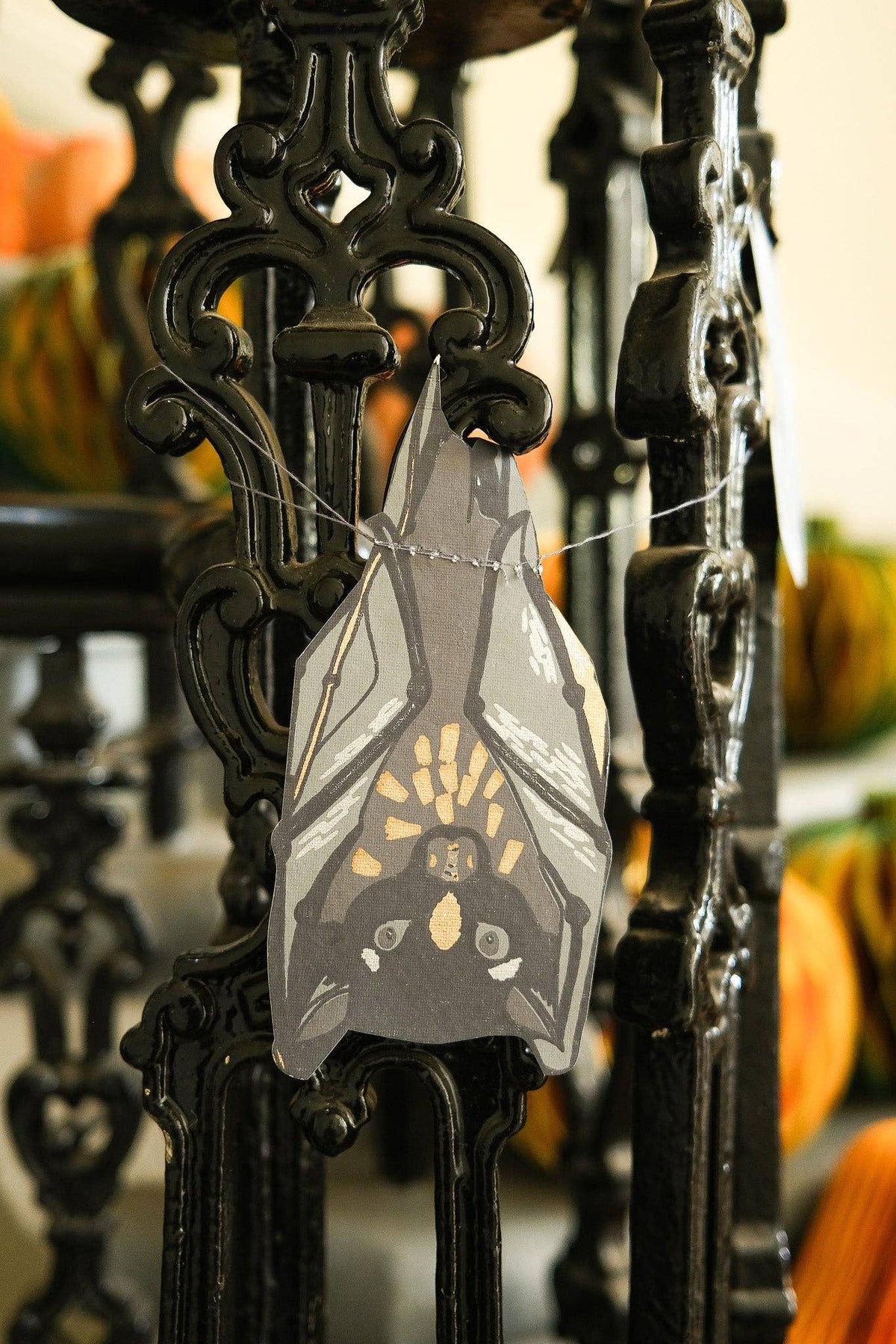 Decorative bat ornament hanging on a black metal stand with pumpkins in the background.