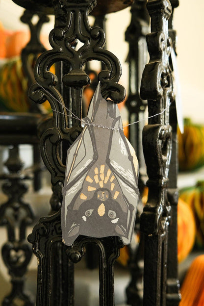 Decorative bat ornament hanging on a black metal stand with pumpkins in the background.