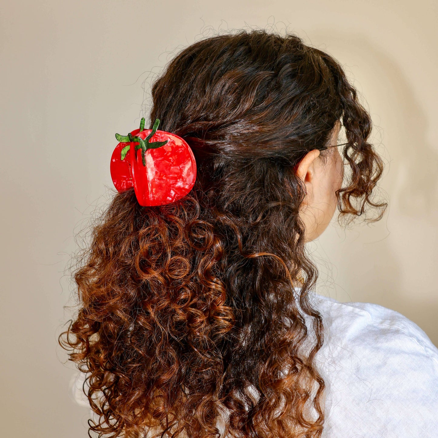 Person with curly hair wearing a red tomato-shaped hair clip on a beige background