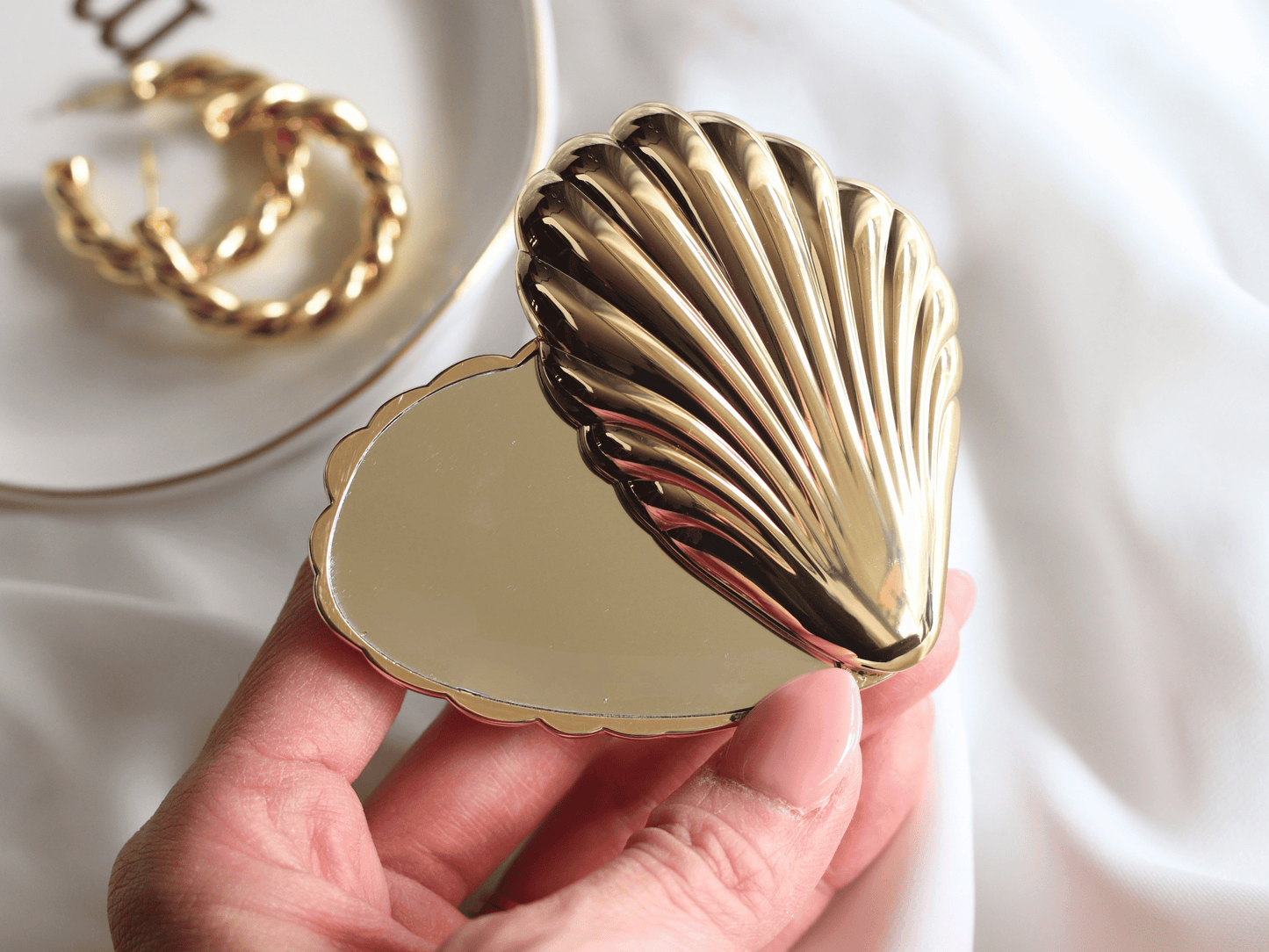 Gold shell-shaped compact mirror held by a hand with a blurred background