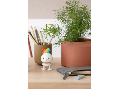 Small white figurine with colorful accents on a desk next to a plant and stationery items.