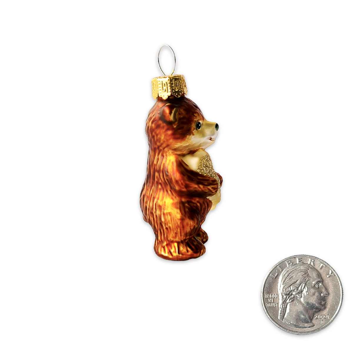 A small glass ornament shaped like a brown bear holding a gold glittery gift box, shown on a white background with a U.S.