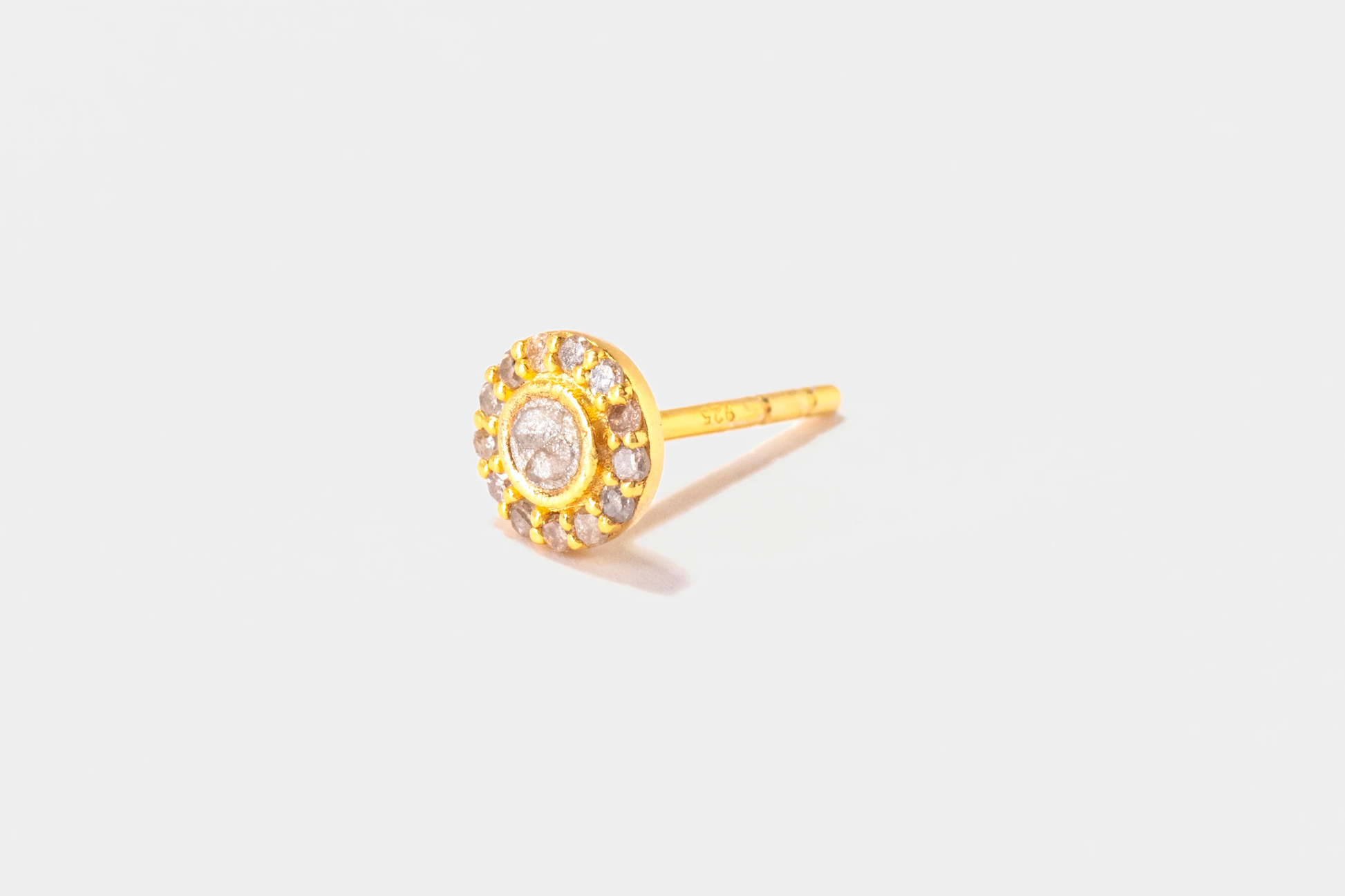 Gold earring with a central gemstone on a light gray background