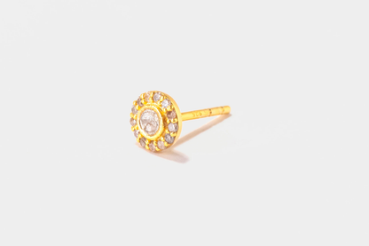 Gold earring with a central gemstone on a light gray background