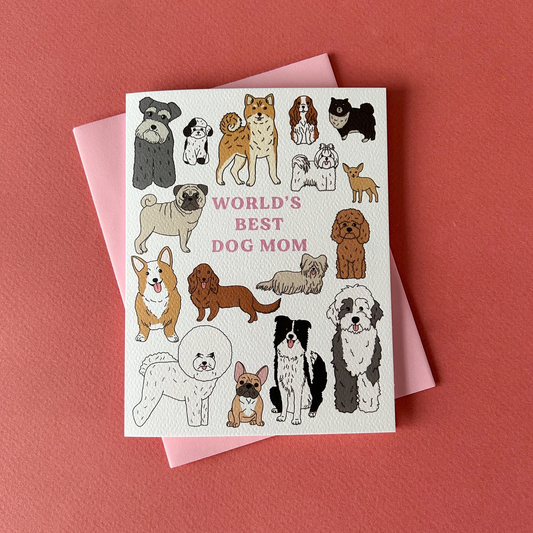 Greeting card with various illustrated dogs and the text 'WORLD'S BEST DOG MOM' across the top, accompanied by a pink envelope, all placed on a red background.