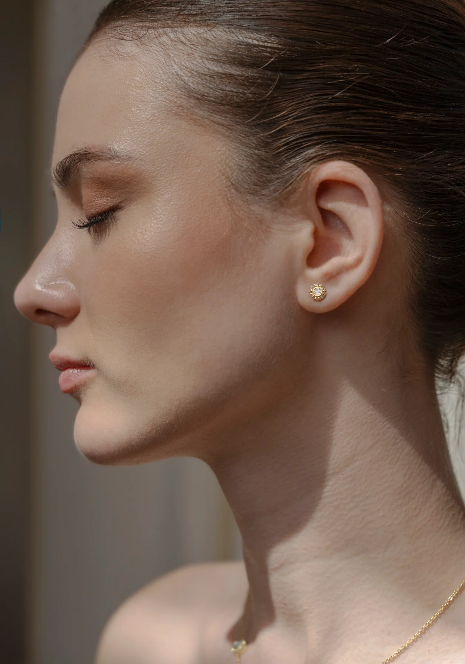 Side profile of a woman wearing small round earrings.