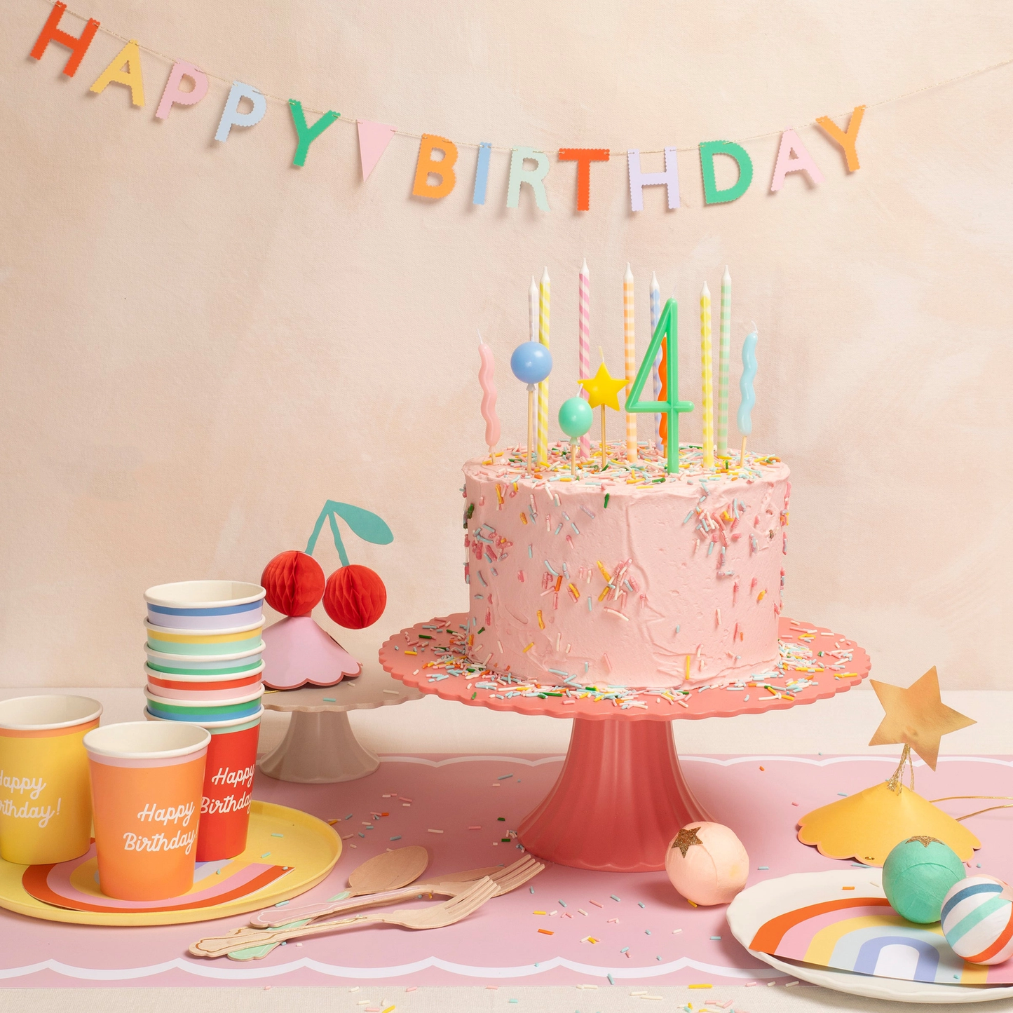 Birthday cake with candles, colorful decorations, and 'Happy Birthday' banner on a table.