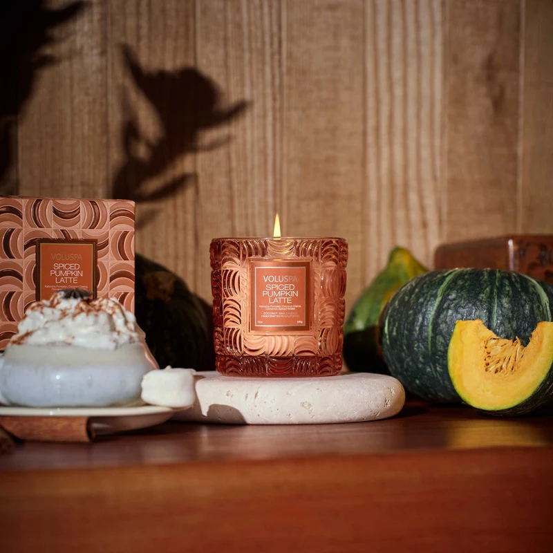 Candle with decorative packaging on a wooden surface with pumpkins and a dessert.