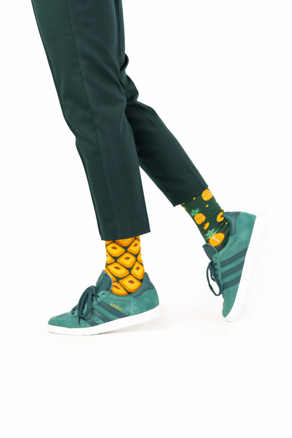 Person wearing green pants, teal sneakers, and pineapple-themed socks on a white background