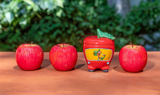 Four red apples with a mug in the center on a wooden surface.